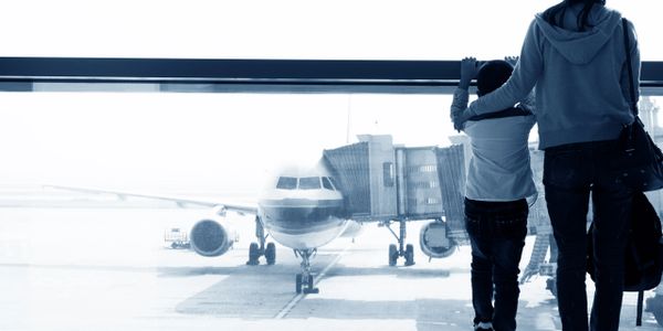 Silhouettes of a child and adult watching a plane at an airport window.