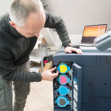 Technician replacing toner cartridges in a large office printer.