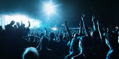 A large crowd enjoying a nighttime outdoor concert with bright stage lights.