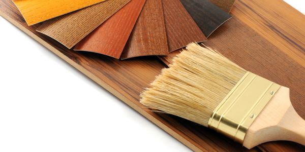 Wood stain samples and a paintbrush on a wooden surface.