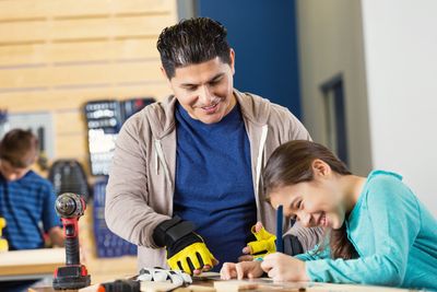 A man teaches a girl woodworking in a workshop.