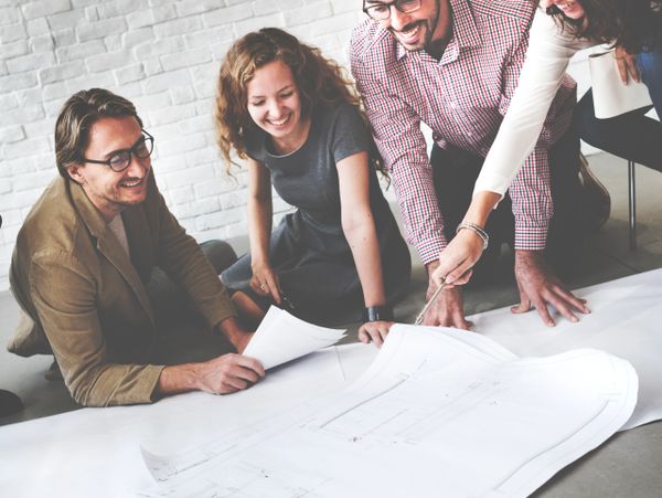 Four colleagues happily reviewing large architectural plans on the floor.