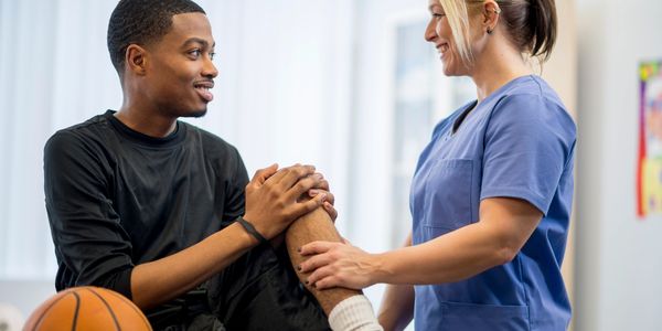 Physical therapist treating a male basketball player with a knee injury.