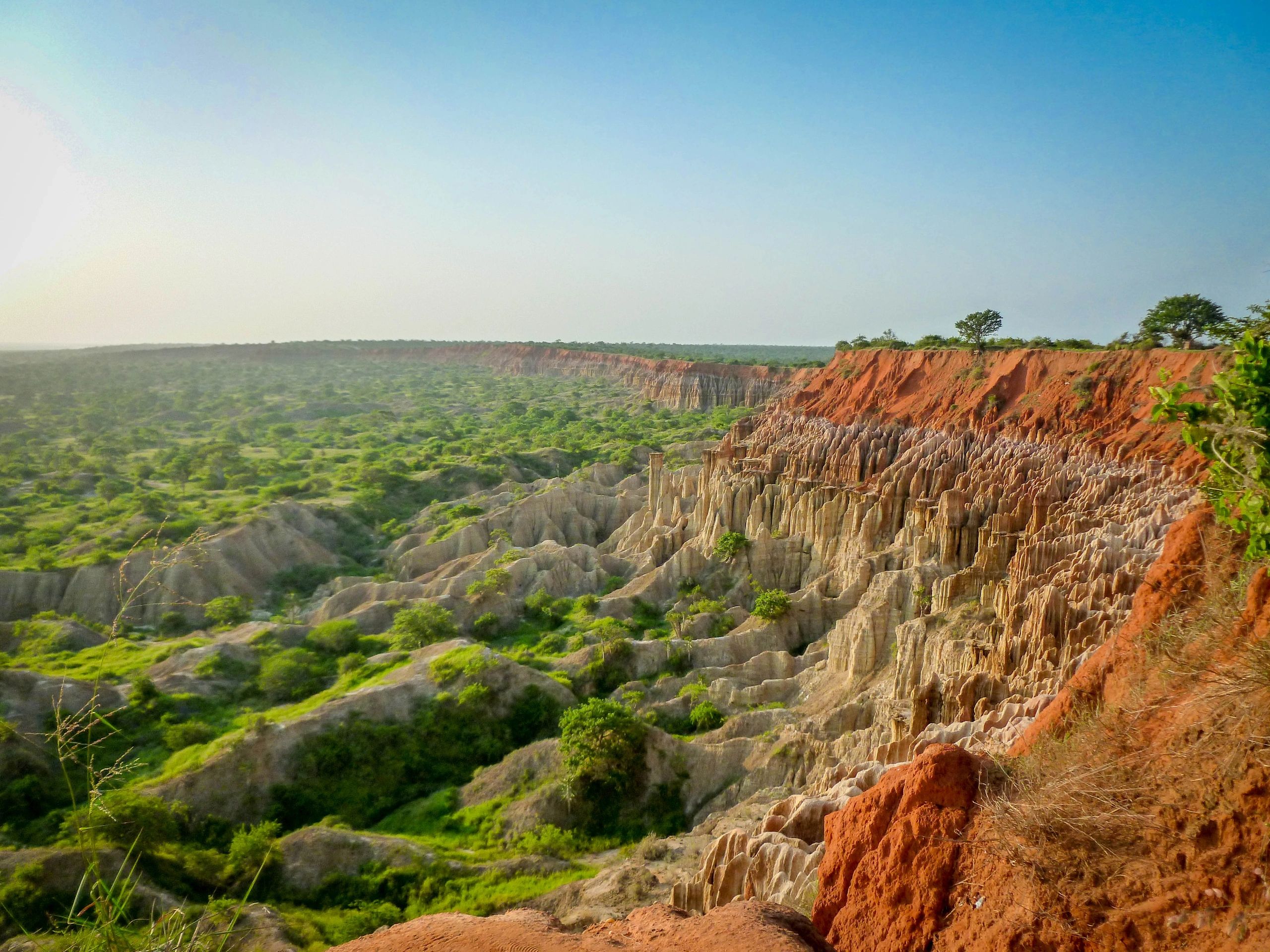 A vast landscape with eroded rock formations and greenery under a clear sky.