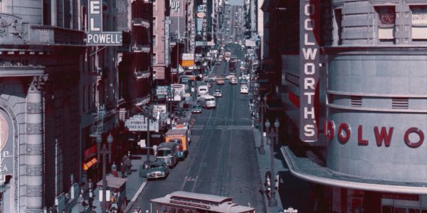 Busy urban street with vintage cars and Woolworths store signage.