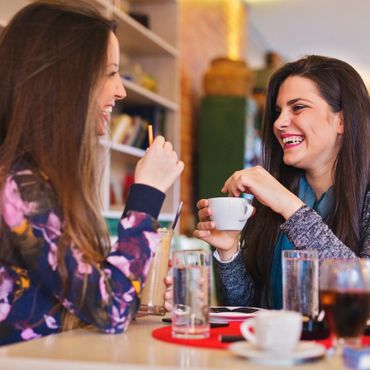 Two women happily chatting over drinks at a café.