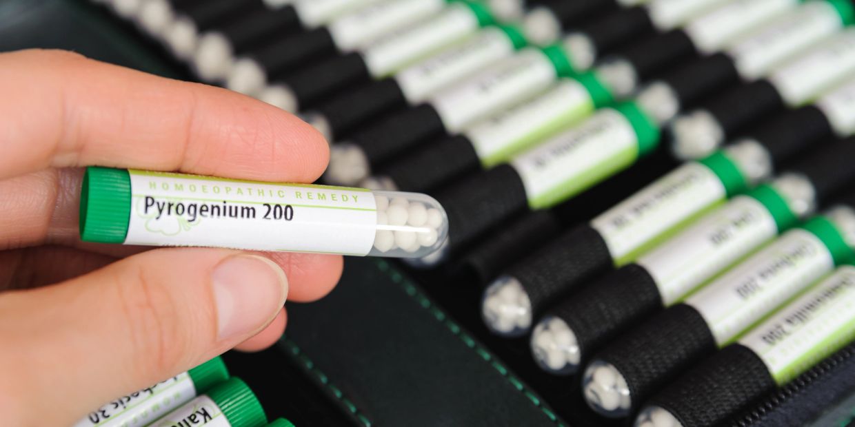 Hand holding a tube of Pyrogenium 200 homeopathic remedy.