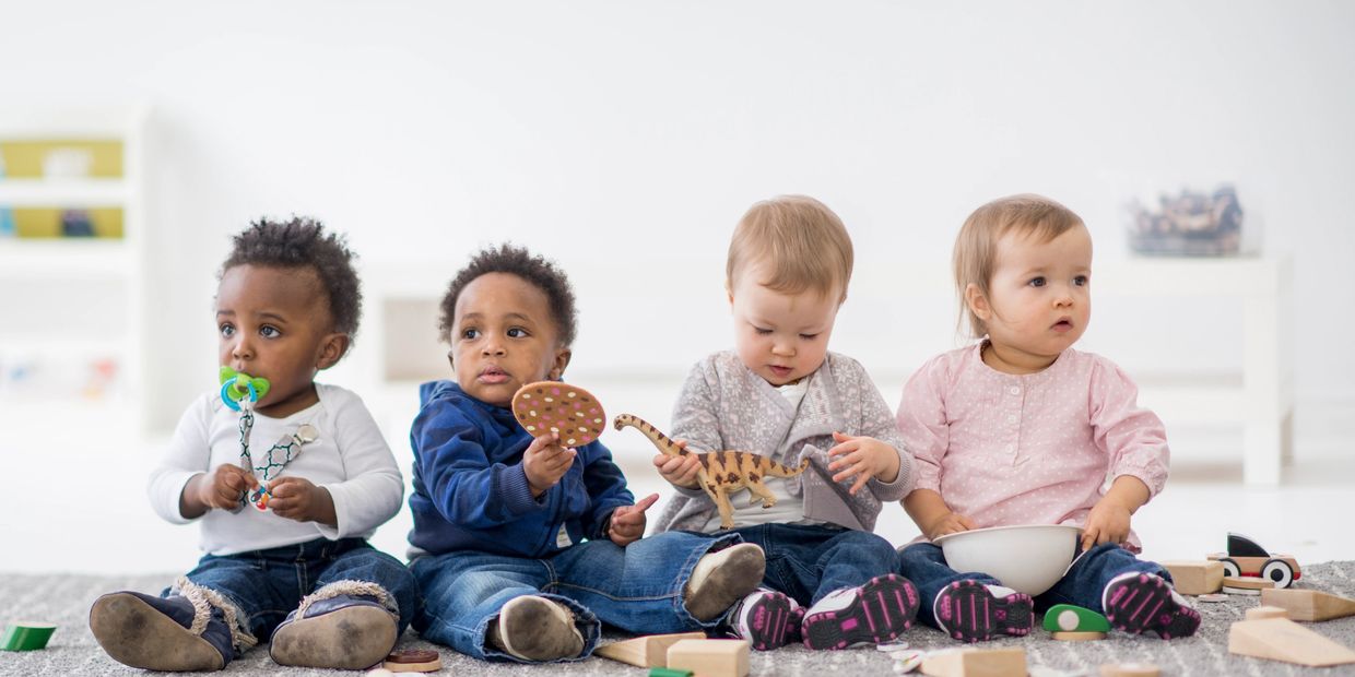 Four toddlers sitting and playing with toys.