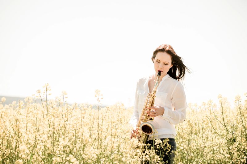 Passion - young  woman playing saxophone in blossoming rapeseed field