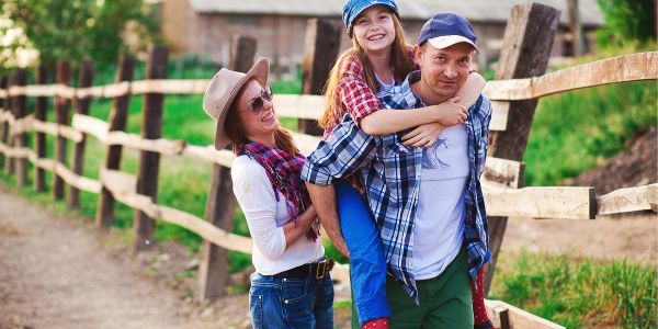 Happy family outdoors with dad giving daughter a piggyback ride.