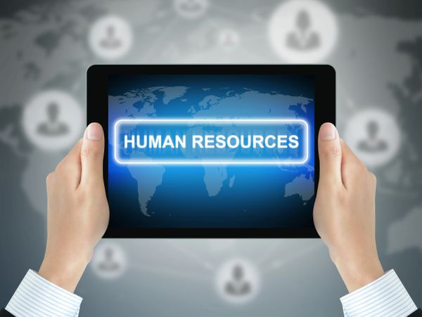 Hands holding a tablet displaying 'HUMAN RESOURCES' with a world map background.