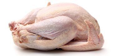 Raw whole chicken placed on a white surface.