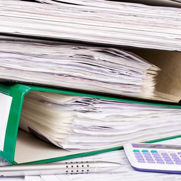 Close-up of thick binders filled with papers, a pen, and a calculator.