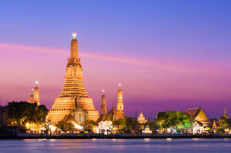 The illuminated temple of Wat Arun on the Chao Phraya river at sunset in Bangkok, Thailand