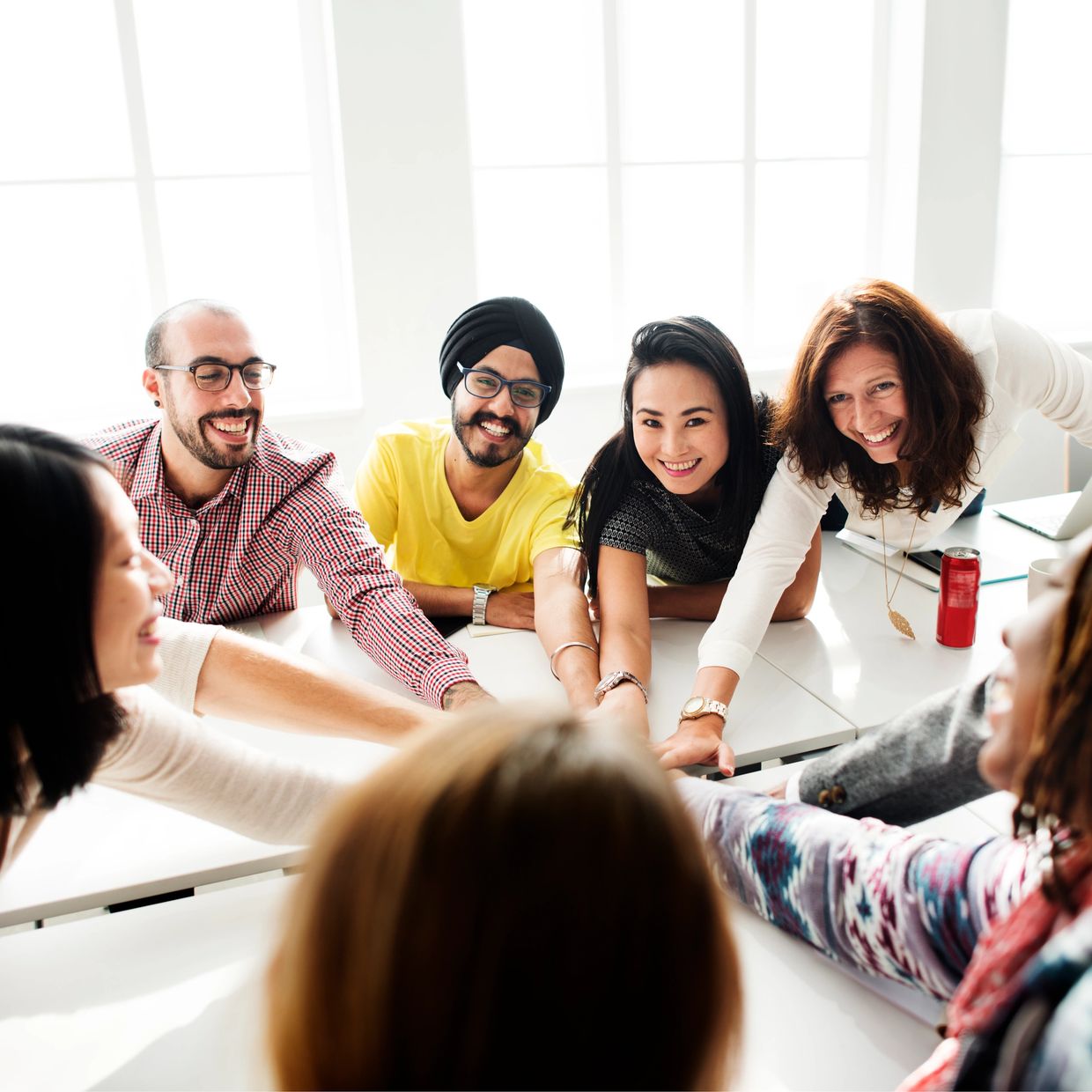 Diverse team joining hands in a collaborative office setting, smiling and motivated.