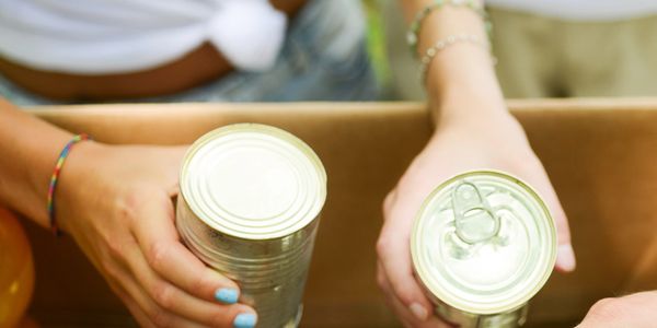 Volunteers sorting canned food for donation in a cardboard box.