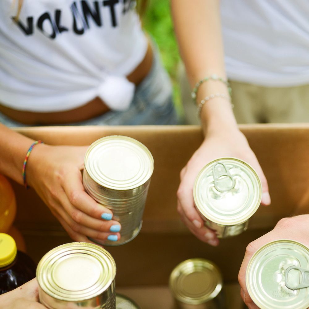 Volunteers sorting canned food for donation in a cardboard box.