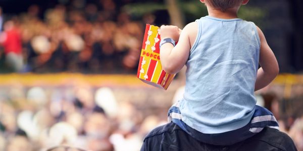 Child on shoulders holding popcorn at crowded event.