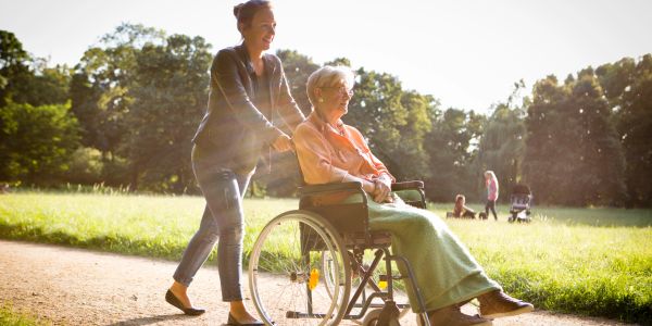 Young woman pushing elderly woman in wheelchair outdoors.