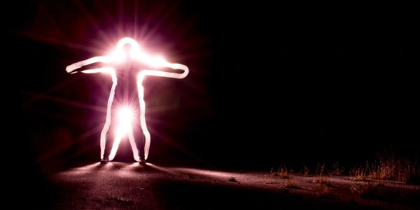 A glowing human figure with outstretched arms illuminated against a dark background.