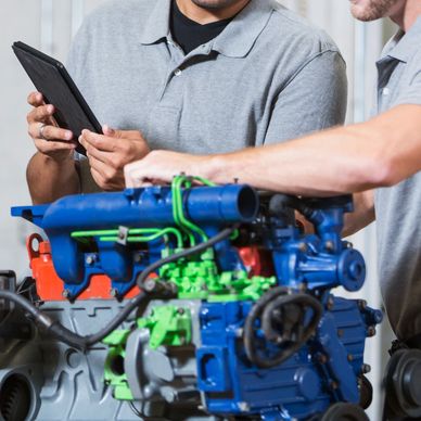 Two people working on a colorful engine, one holding a tablet.