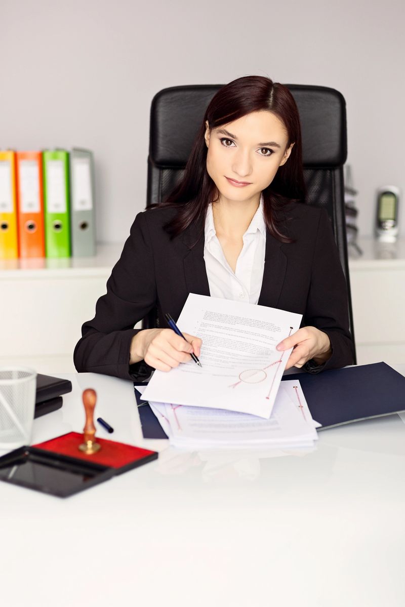 Woman notary public holding pen and pointing at signature place on a contract document