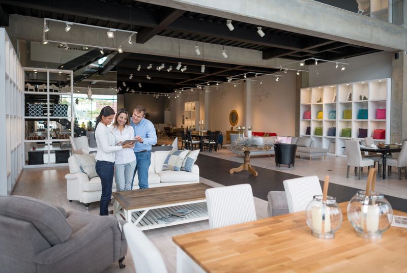 Couple shopping at a furniture store and talking to saleswoman while looking at a catalog on a tablet computer