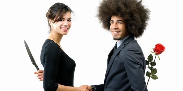 A couple shaking hands with hidden motives behind backs.