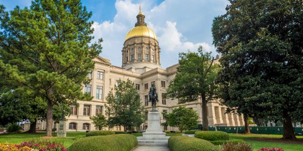 State capitol building with a golden dome and statue in front.
