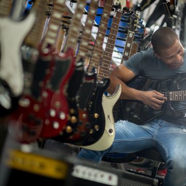 Man sitting in a guitar shop playing an electric guiter