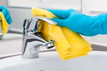 Person cleaning a faucet with a yellow cloth.