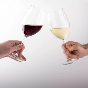 Two hands clinking red and white wine glasses.
