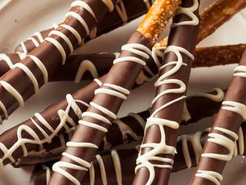 Chocolate-dipped pretzel sticks drizzled with white chocolate on a white plate.