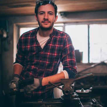 Man in plaid shirt working with a grinder in a workshop.