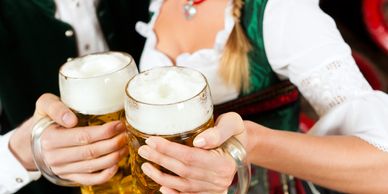 Two people in traditional attire clinking beer mugs filled with frothy beer.