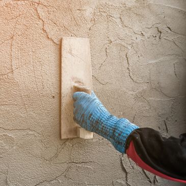 Hand smoothing wet plaster on a textured wall with a trowel.