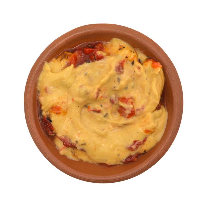 Top view of a small bowl with a serving of hummus with red peppers isolated on a white background.