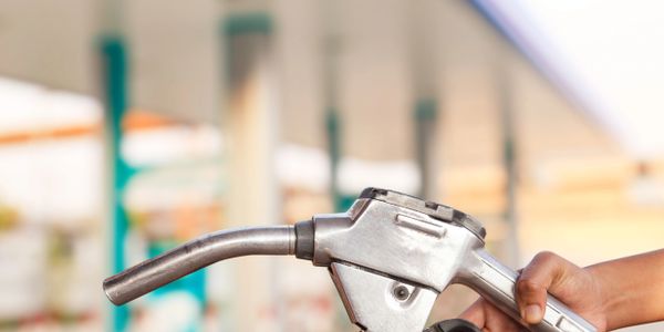 Hand holding a fuel pump nozzle at a gas station.