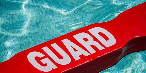 Red lifeguard float in clear blue pool water.