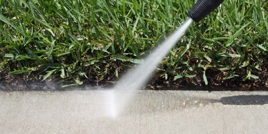 A pressure washer cleaning a concrete sidewalk near grass.