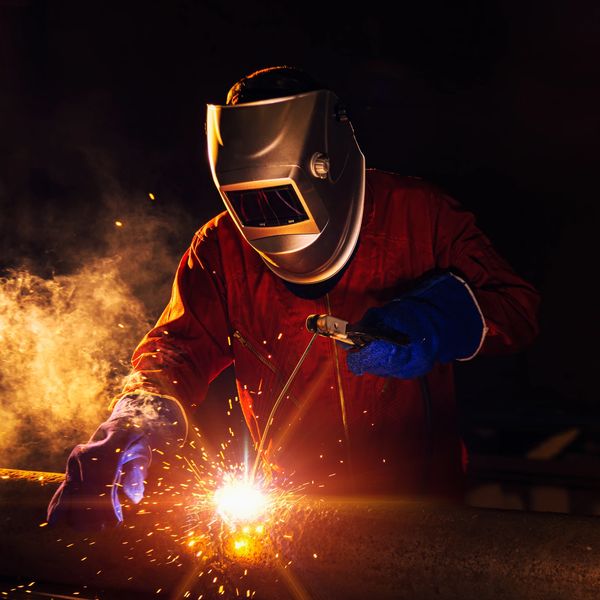 Welder in protective gear working on metal with sparks flying.