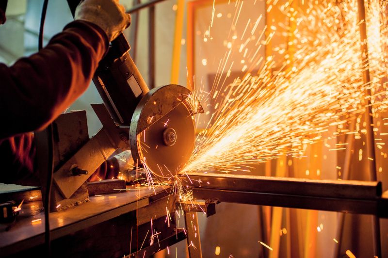 A man working with electric grinder tool  on steel structure in factory, sparks flying
