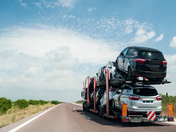 Car carrier truck transporting multiple new cars on an open road.