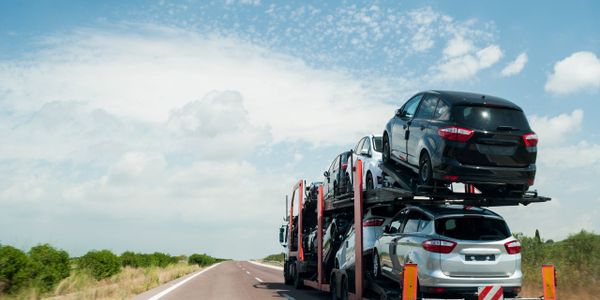 Car carrier truck transporting multiple vehicles on a highway under a blue sky.