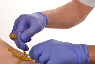 Hands with gloves tying a tourniquet on an arm.