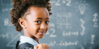 Smiling child with backpack in front of chalkboard with math equations.