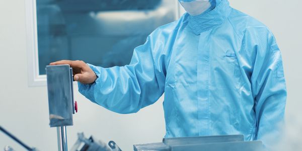 Technician operating machinery in a cleanroom wearing protective gear.