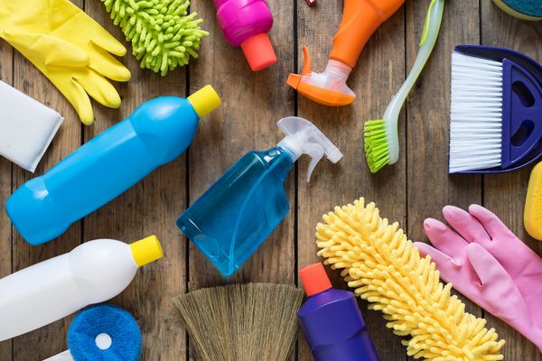 Various colorful cleaning supplies and gloves on a wooden surface.