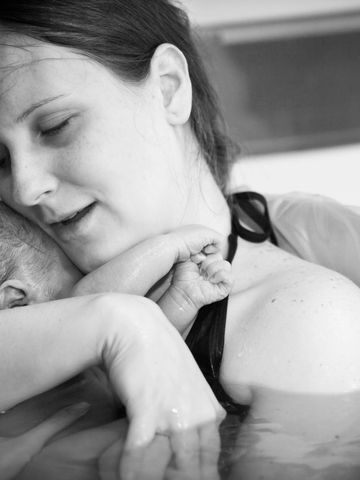 A mother tenderly holds her newborn in water, sharing a peaceful moment.