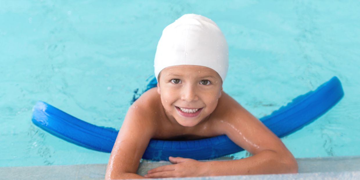 Smiling boy in swimming cap at pool edge.